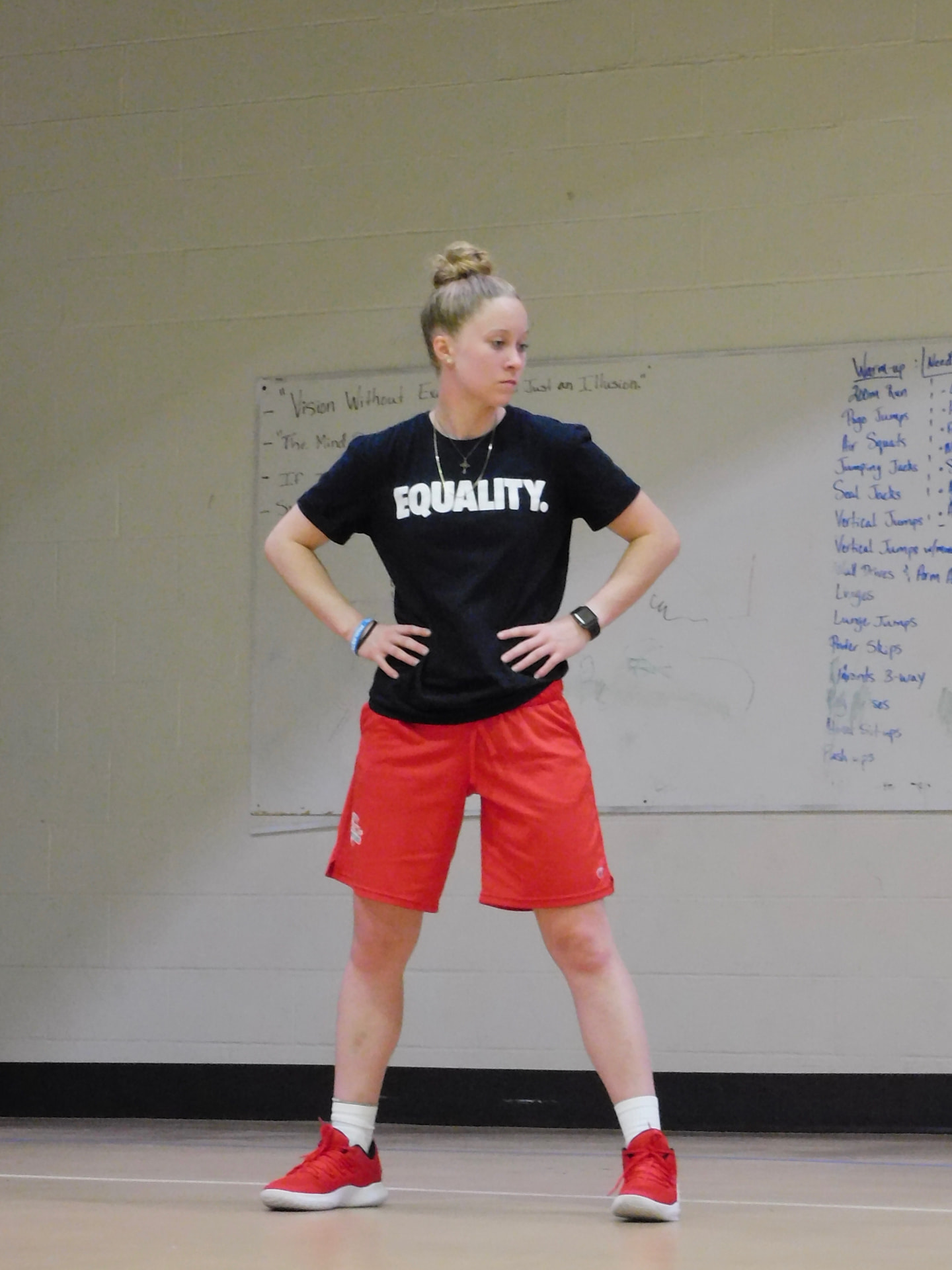 Hannah Mortimer coaching in a gym, wearing a black EQUALITY shirt and red shorts